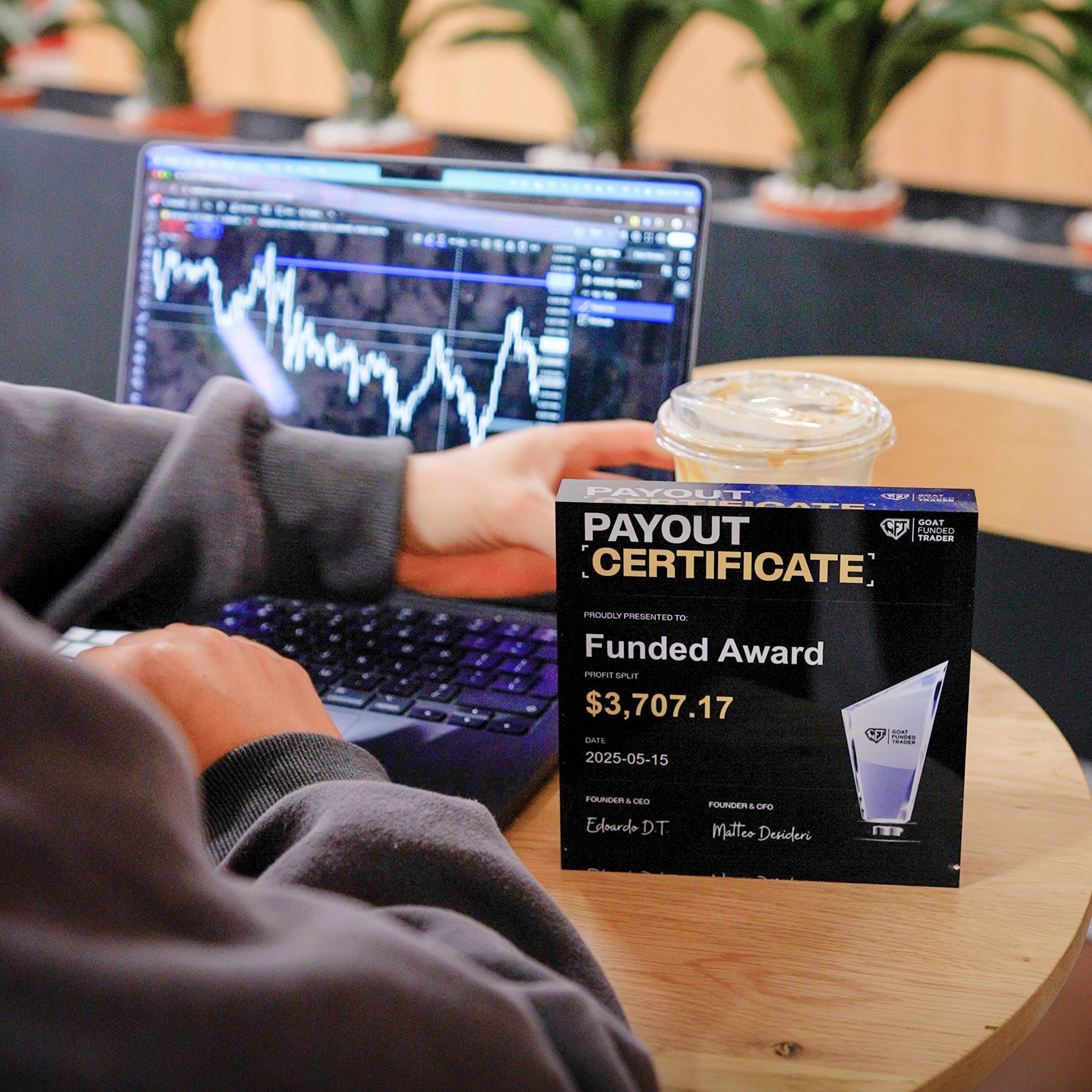 Person using a laptop to trade with a 'Payout Certificate' displayed in front from Goat Funded Trader