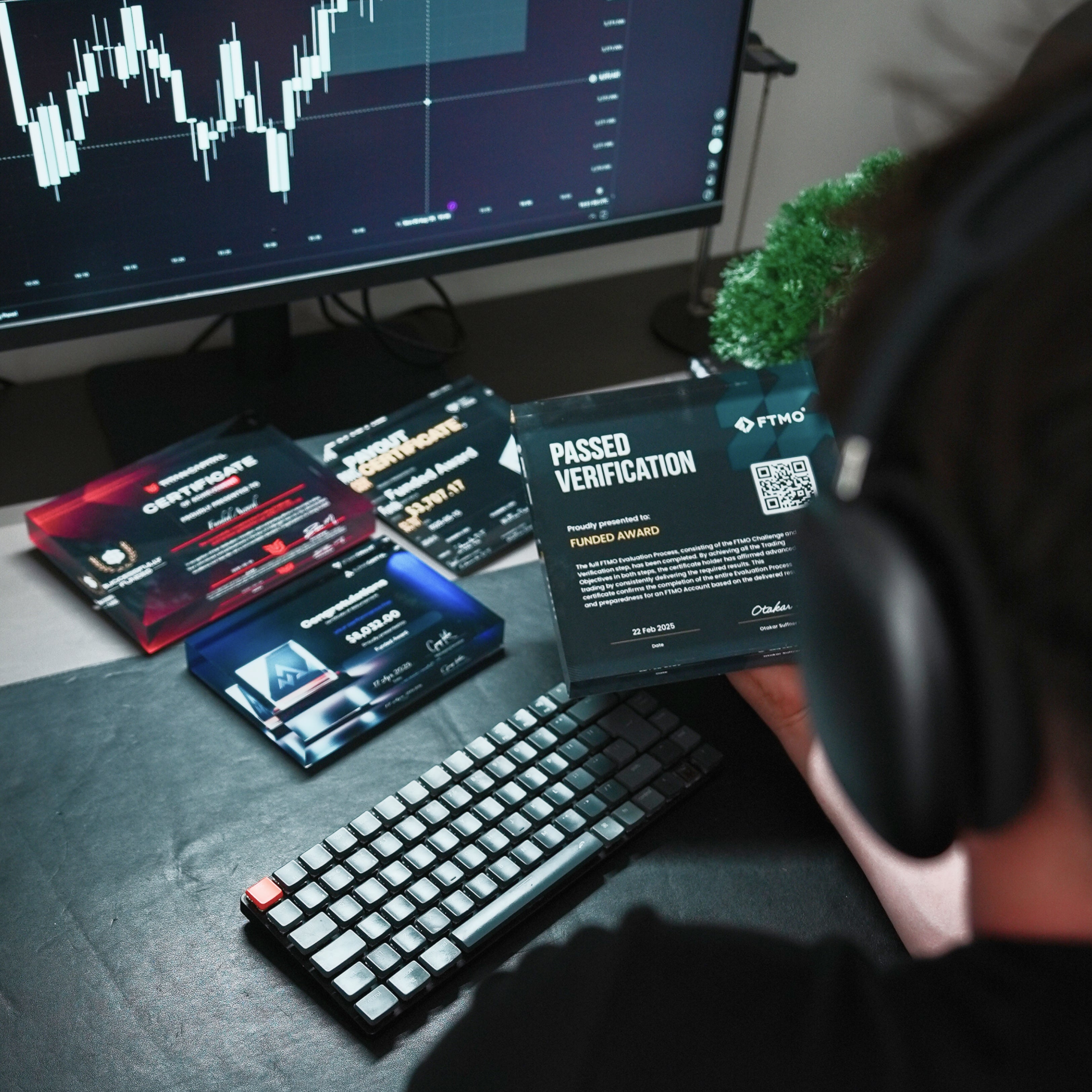 Person wearing headphones at a desk with multiple verification Awards from FTMO,ALPHA CAPITAL,TITANCAPITAL and a computer screen displaying stock market data.