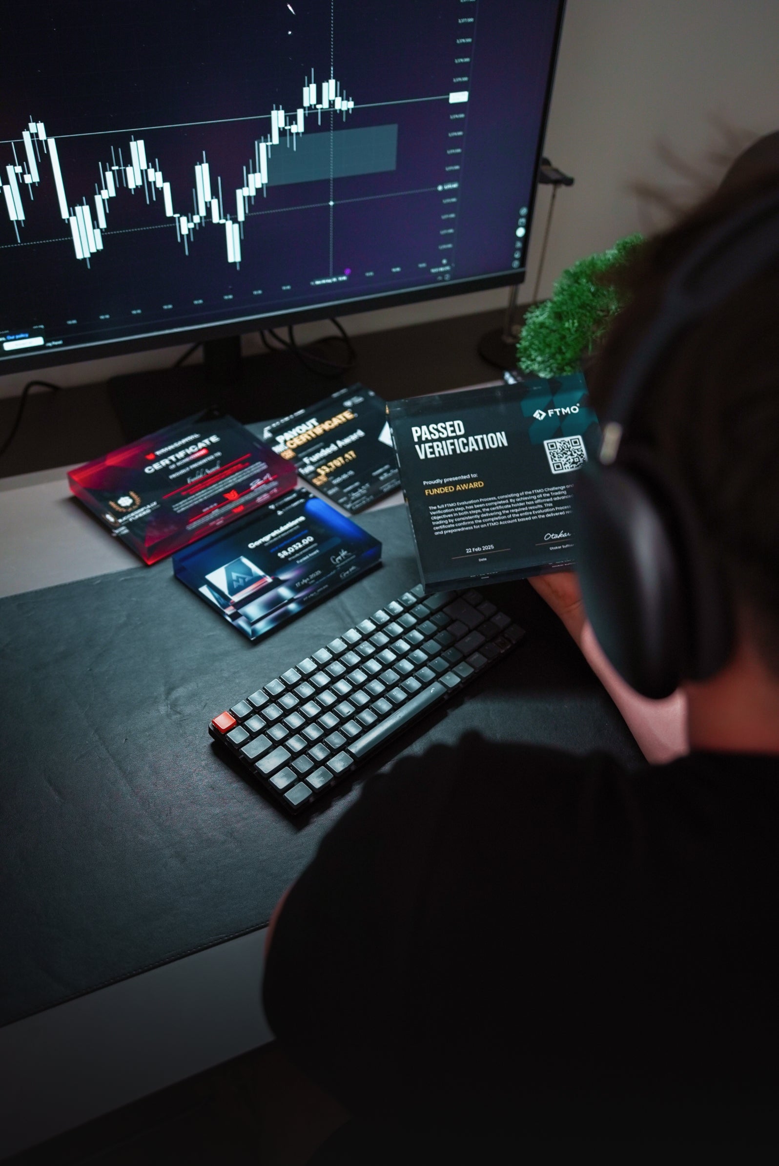 Trader sitting on his desk with tradingview charts and holding an FTMO Funded Award plaque
