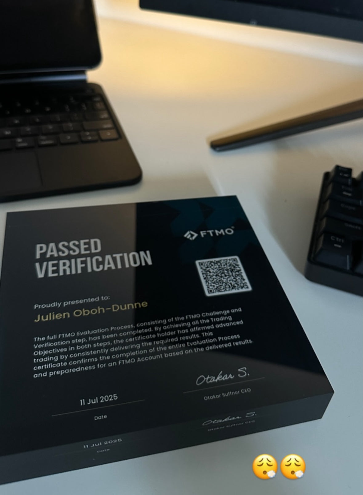 FTMO verification certificate on a desk with a laptop and keyboard in the background