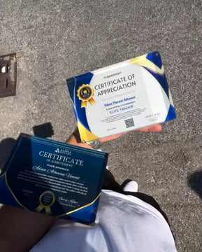 Two funded certificates, one of Alpha Capital, the other is Fundednext prop firm held against a concrete floor background
