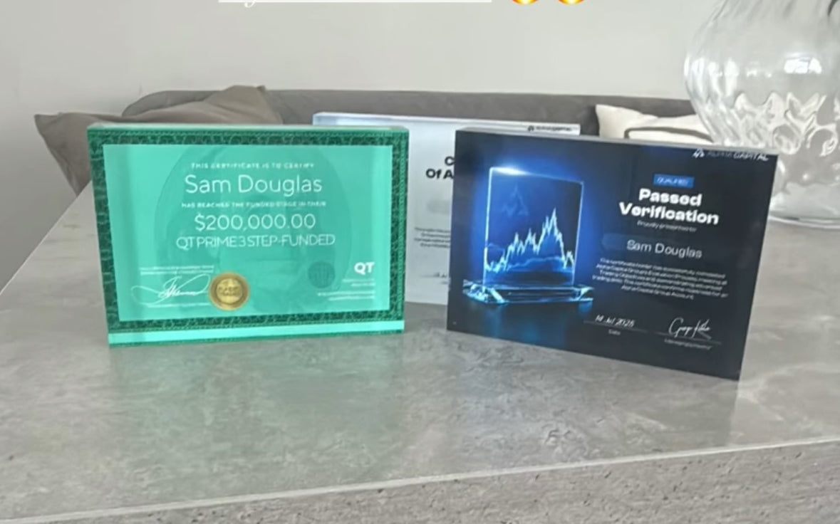 Two framed certificates on a glass surface, one is a pass chalenge of QT Funded and the other is beloge to Alpha Capital prop firm