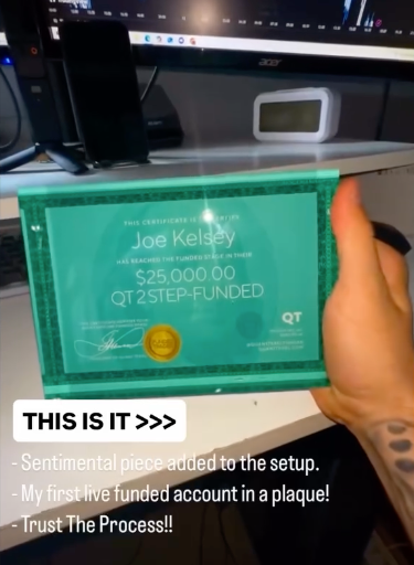 Hand holding a  QT trading funded certificate from Funded Award with text on a desk