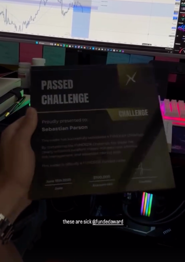 Hand holding a Passed Challenge-funded certificate from Funded Award in front of a computer screen with trading software.